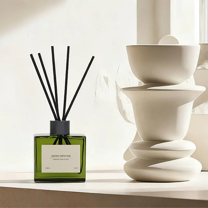 Green glass aroma diffuser with black reeds beside stacked white ceramic decor - modern home zen style